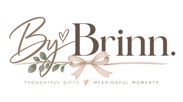 A digital logo graphic for 'By Brinn.' featuring elegant brown script and serif typography, a beige ribbon bow, green leaves, and the tagline 'THOUGHTFUL GIFTS MEANINGFUL MOMENTS' on a solid white background.